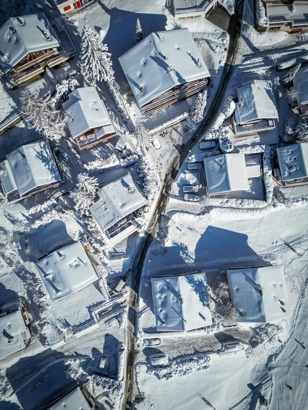 Top down aerial view of a cleared road curving between snow covered chalet roofs and pine trees in Verbier